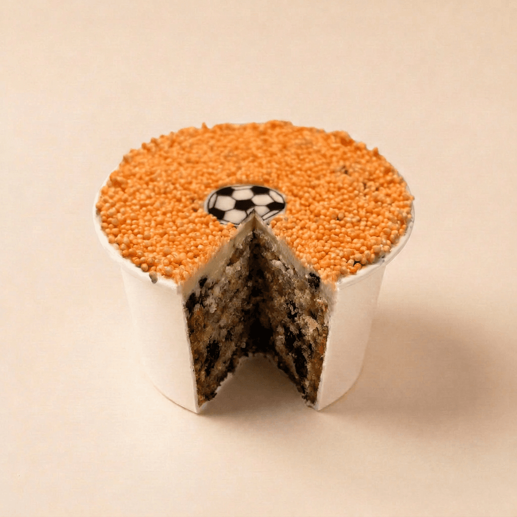 Bovenaanzicht van de WK Special dotcake met romige witte frosting, oranje spikkels en een voetbaldecoratie centraal bovenop.