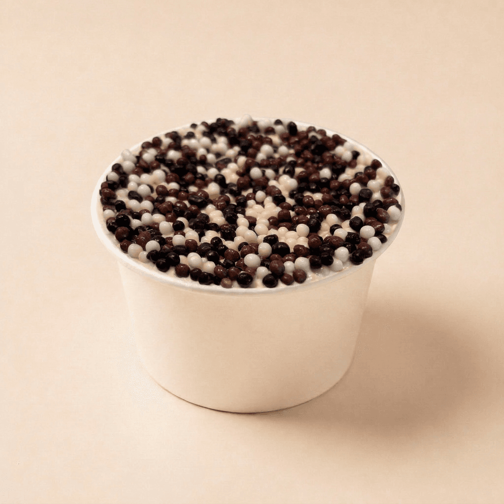 Chocolade dotcake in een wit bakje, afgewerkt met romige roomkaasfrosting en royaal bedekt met krokante chocolade dots van melk- en witte chocolade