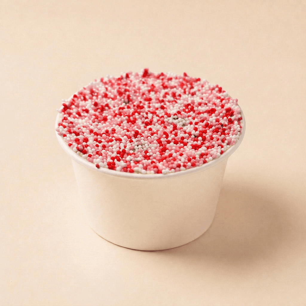 Red velvet dotcake in een wit bakje, afgewerkt met romige roomkaasfrosting en volledig bedekt met rood-roze spikkels voor een feestelijke uitstraling.