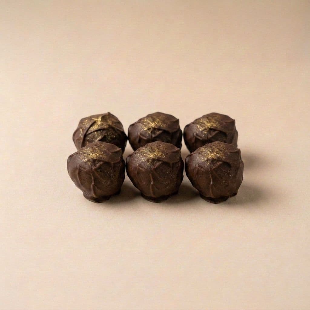 Zes Dubai Choco Dough balletjes van melkchocolade met subtiele gouden afwerking op een neutrale achtergrond.