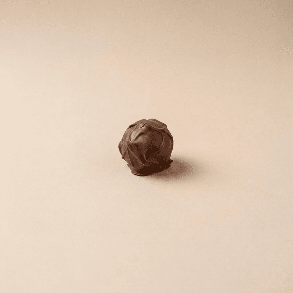 Eén ronde ChocoDough-bal met een romige melkchocoladecoating staat centraal op een zachte beige achtergrond. De ambachtelijke, golvende chocoladelaag geeft het product een luxe en smeuïge uitstraling met minimale, stijlvolle presentatie.