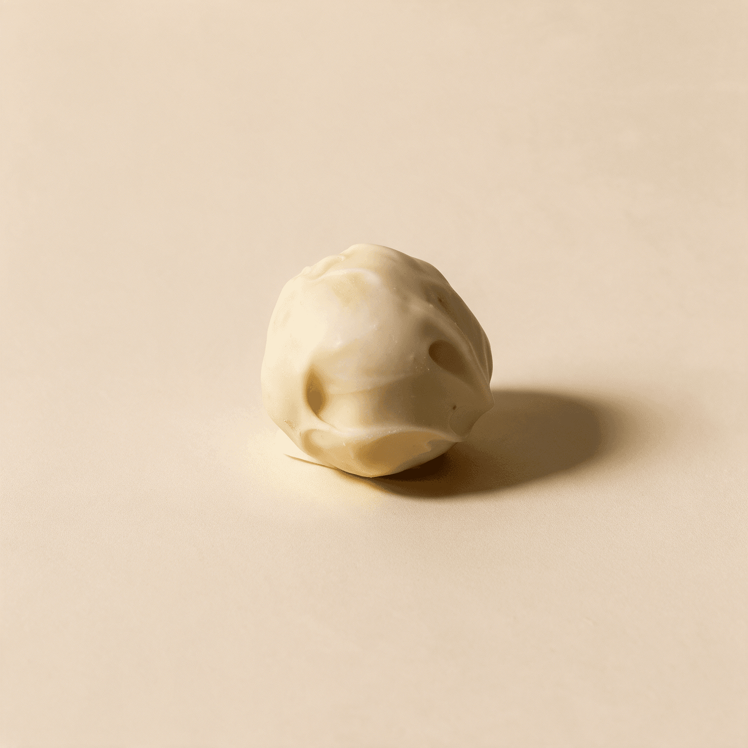 Close-up van één lemon cookie dough ball met een glanzende, grillige laag witte chocolade, op een zachtbeige achtergrond.